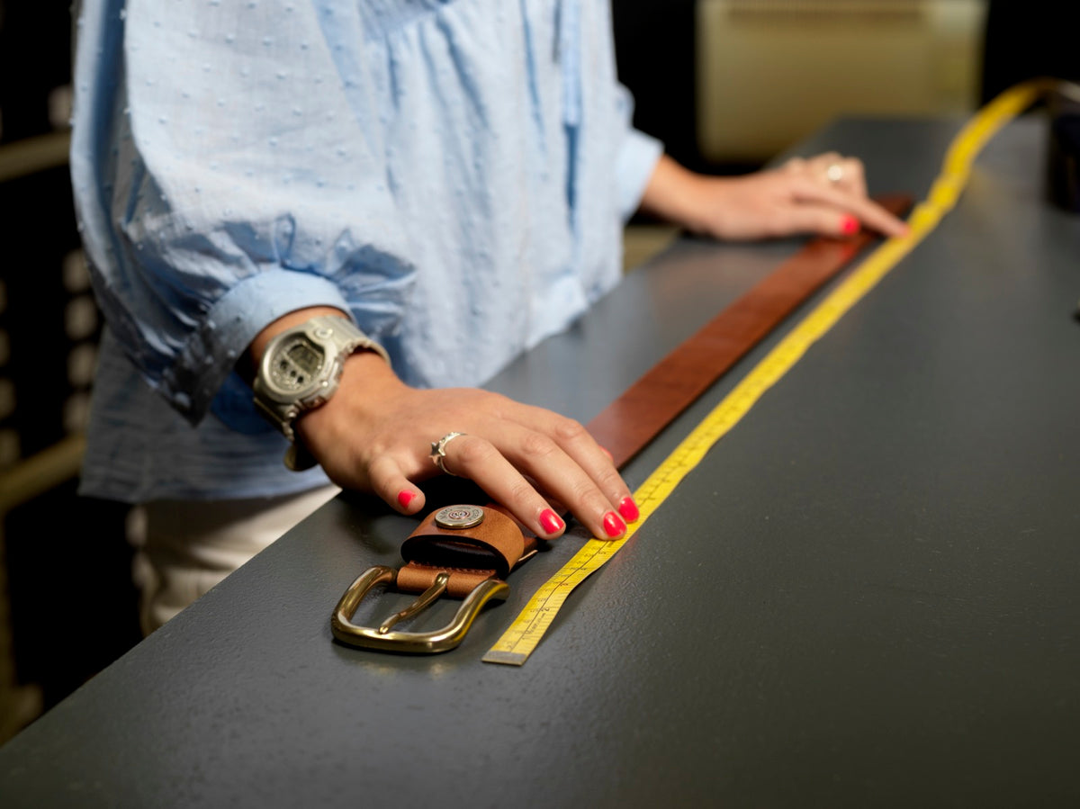 A leather belt being measured with a tape measure in the Mackenzie &amp; George workshop