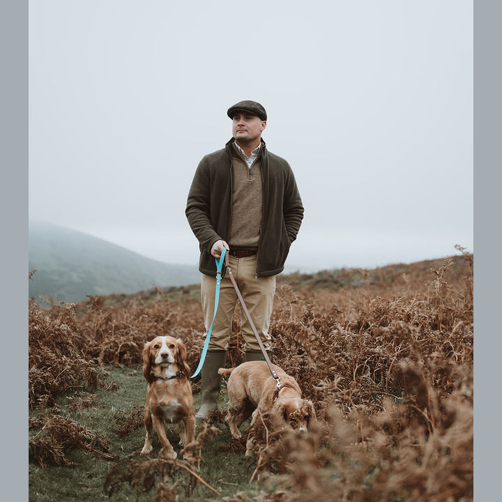 Handler walking dogs on turquoise Biothane leads across moorland