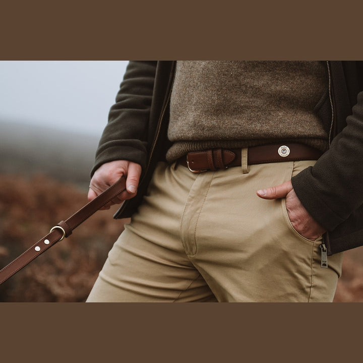 Handler holding a brown leather dog lead outdoors