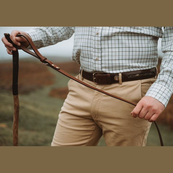 Handler holding a brown leather lead across the body