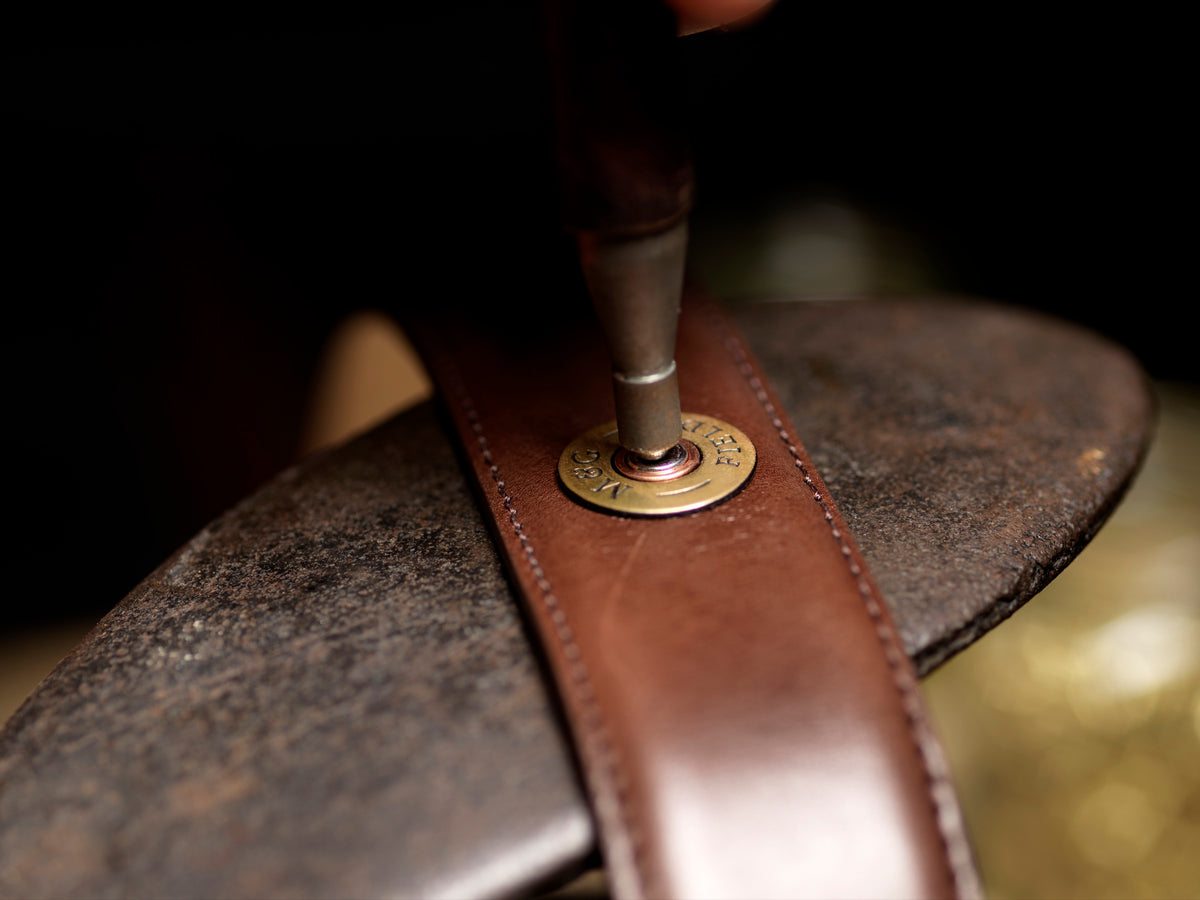A cartridge-style rivet being set into a leather belt in the M&G workshop